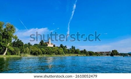 Panoramic view from the side of the lake Constance, Bodensee, on the historic Baroque Birnau basilica. In the foreground - blue lake, green trees and vineyards on the hills. Germany.