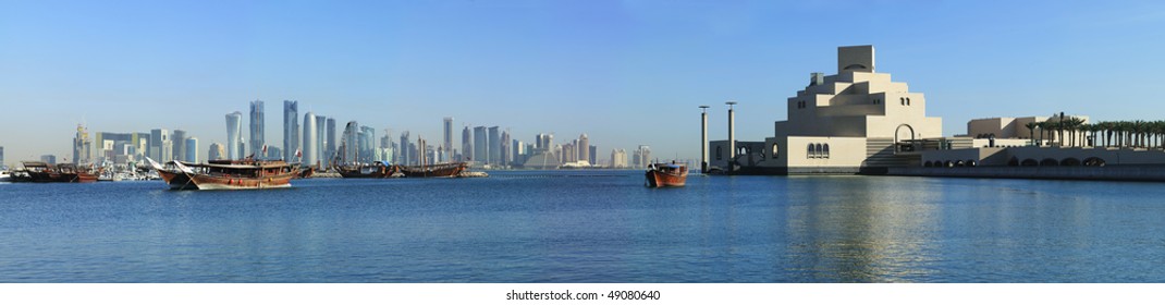 A panoramic view of the skyline of Doha, seen from the corniche with moored dhows and the Museum of Islamic art in the foreground