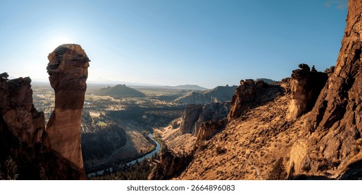 Panoramic view of Smith Rock State Park in Oregon, showcasing towering rock formations and a winding river under a clear blue sky.