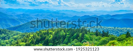 A panoramic view of the Smoky Mountains from the Blue Ridge Parkway in North Carolina. Blue sky with clouds over layers of green hills and mountains. North Carolina. Image for banner and web header.