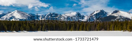 Panoramic view of the snow covered Rocky Mountains on a sunny, winter day with a forest and frozen lake view in Rocky Mountain National Park near Estes Park, Colorado