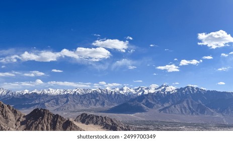 A panoramic view of a snow-capped mountain range towering over a valley with a small town nestled within it.
