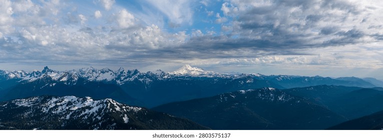 Panoramic view of snow-capped mountains and dramatic clouds over the coastal ranges of British Columbia, Canada.