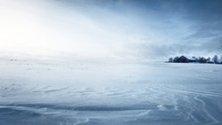 Панорамный вид на заснеженное поле после метели на закате. Человеческие следы в свежем снегу. Старый деревенский деревянный дом на заднем плане. Ледяная пустыня. Тема глобального потепления. Лапландия