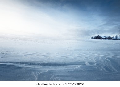 Panoramic view of the snow-covered field after a blizzard at sunset. Human tracks in a fresh snow. Old rustic wooden house in the background. Ice desert. Global warming theme. Lapland, Finland