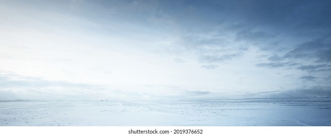 Panoramic view of the snow-covered field after a blizzard at sunset. Human tracks in a fresh snow. Ice desert. Dramatic cloudscape. Global warming theme. Lapland, Finland