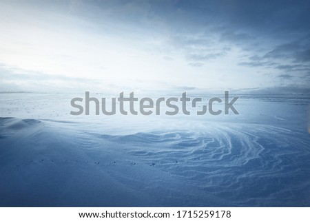 Panoramic view of the snow-covered field after a blizzard at sunset. Human tracks in a fresh snow. Ice desert. Dramatic cloudscape. Global warming theme. Lapland, Finland
