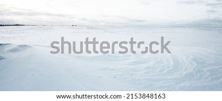 Panoramic view of the snow-covered field after a blizzard at sunset. Human tracks in a fresh snow. Ice desert. Dramatic cloudscape. Global warming theme. Lapland, Finland