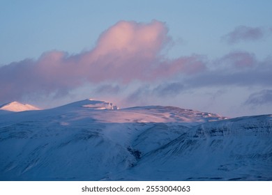 Panoramic view of snow-covered mountain range under a blue sky with pink-tinged clouds illuminated by setting sun.