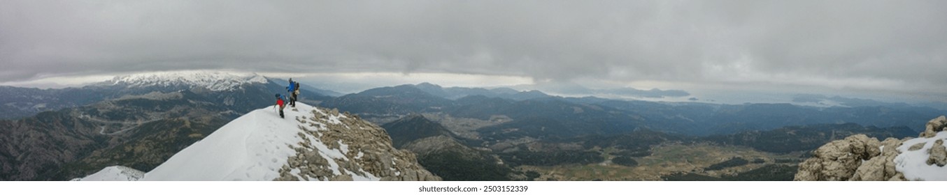 panoramic view from a snow-covered mountain ridge, where three adventurous hikers are making their way along the snowy path. The hikers are dressed in winter gear, including jackets and backpacks - Powered by Shutterstock