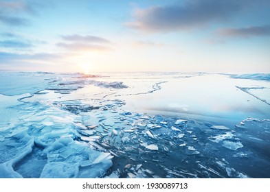 Panoramic view of the snow-covered shore of the frozen Baltic sea at sunset. Ice fragments close-up. Colorful cloudscape, soft sunlight. Symmetry reflections on the water. Christmas, seasons, winter