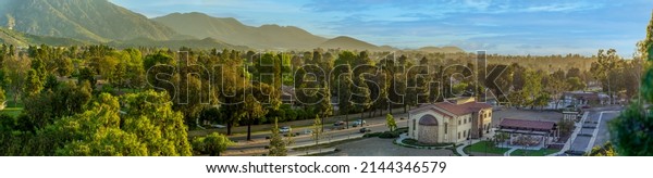 Panoramic view\
of southern California valley with mountains and church with Avenue\
of trees and cars in urban \
setting