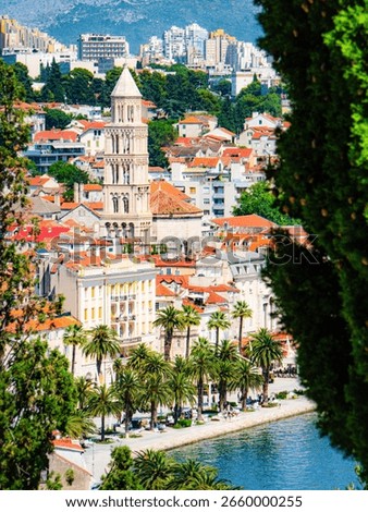 Panoramic view of Split, Croatia, featuring the Cathedral of Saint Domnius bell tower, red-tiled rooftops, palm-lined promenade, Adriatic Sea, and hills in the background.