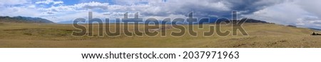 Panoramic view to steppe with mountains and cloudy sku on background.