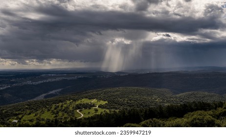 Panoramic view of sun rays shining through rainclouds showing thefalling rain in Northern Israel looking towards the Mediterranean Sea from Muhraqa viewpoint.
