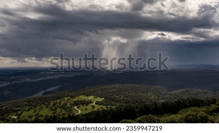 Panoramic view of sun rays shining through rainclouds showing thefalling rain in Northern Israel looking towards the Mediterranean Sea from Muhraqa viewpoint.
