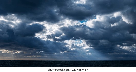 Panoramic view of the sunrays through the stormy clouds over the dark sea