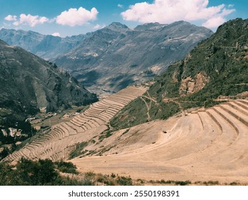 Panoramic view of terraced fields in the Andes mountains of Peru, surrounded by rugged peaks and a bright blue sky. - Powered by Shutterstock