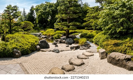 Panoramic view of the tranquil Japanese garden in Loki-Schmidt-Garten, Hamburg, featuring a serene pond surrounded by neatly manicured trees, bushes and a path with zen-like lines in the summer sun. - Shutterstock ID 2271340215