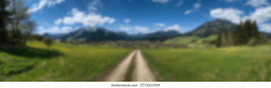 A panoramic view of a tranquil landscape featuring a dirt path winding through a vibrant green field, with imposing mountains in the distance and a bright blue sky overhead.