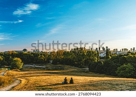 Panoramic view of two people sitting on a vast park hill overlooking a distant city skyline