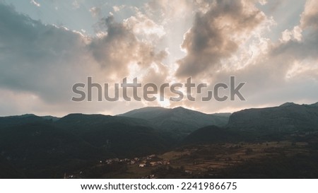 panoramic view of a valley surrounded by hills at sunset with the sun obscured by clouds