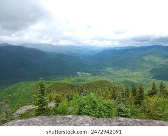 A panoramic view of a valley unfolds from a mountain peak. Lush green meadows and forests sprawl across the valley floor, with a winding river snaking through the center. Rugged mountains rise in the  - Powered by Shutterstock