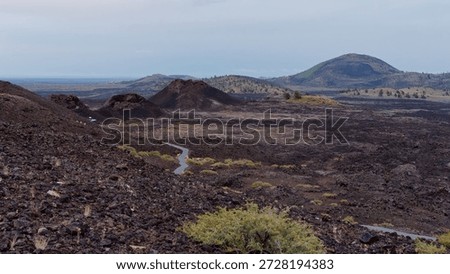 Panoramic view of the volcanic landscape featuring Big Cinder Butte and winding trails through the North Crater lava flow,  at Craters of the Moon National Monument, Idaho, USA