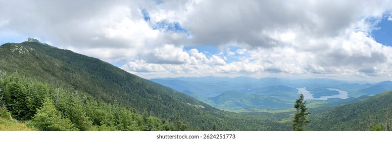 Vista panorámica desde Whiteface Mountain en Adirondacks, Nueva York, con nubes dramáticas, picos verdes ondulantes y la silueta sinuosa del lago Placid en el valle de abajo.