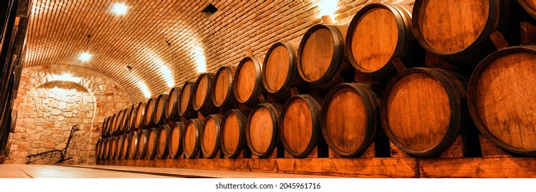 Panoramic View Of Wine Barrels In The Old Basement Of A Winery. Cellar Of Wine Vault With Brick Walls.