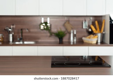 Panoramic View Of Wooden Countertop With Empty Induction Surface On Ceramic Glass Stove Against Blurred Copy Space Background With Modern Interior And White Kitchen Cupboards