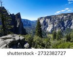 Panoramic view of Yosemite Valley with dramatic granite cliffs, pine forest and clear blue sky on a sunny day.