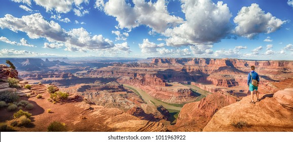 Panoramic view of young hiker standing on a cliff in in scenic Dead Horse Point State Park enjoying the view on a beautiful sunny day with blue sky and dramatic clouds in summer, Utah, USA