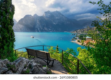 Panoramic viewpoint from a bench overlooking Torbole sul Garda and the turquoise water of the Upper Lake Garda (Alto Garda). Mountain and a cruise boat, Trentino, Italy