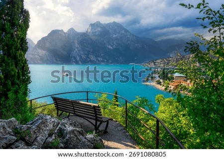 Panoramic viewpoint from a bench overlooking Torbole sul Garda and the turquoise water of the Upper Lake Garda (Alto Garda). Mountain and a cruise boat, Trentino, Italy