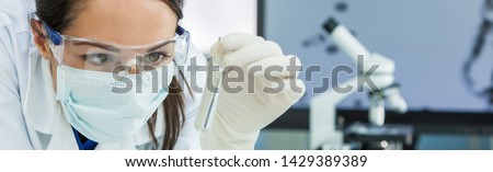 Panoramic web banner female medical or research scientist or doctor using looking at a test tube of clear solution in a lab or laboratory. Header panorama.