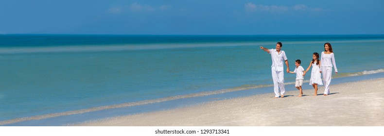 Panoramic Web Banner Happy Family Of Mother, Father And Two Children, Son And Daughter, Walking Holding Hands And Having Fun In The Sand On A Sunny Beach