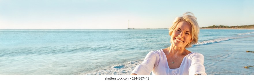 Panoramic web banner happy senior woman dancing and reaching with her hands on a deserted tropical beach, s3niorlife - Powered by Shutterstock