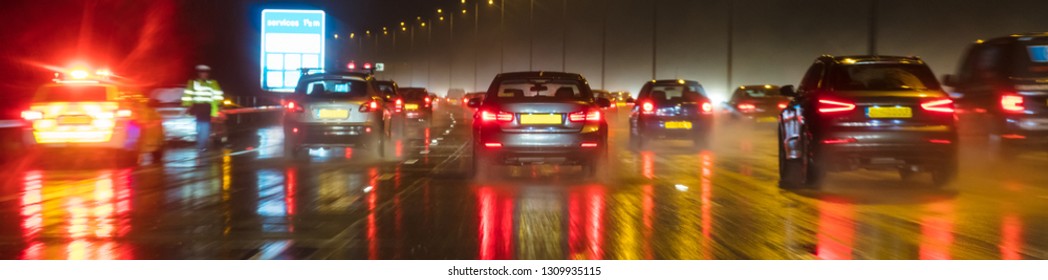 Panoramic Web Banner Motion Blurred Photograph Of Traffic At In Night In The Rain On A British Motorway With Police Officer And Car