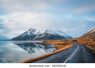 Panoramic winter photo of road leading along coast of lake to volcanic mountains. High rocky peaks covered with snow layer mirroring on water surface. Driver's point of view on Ring road, Iceland. - Powered by Shutterstock