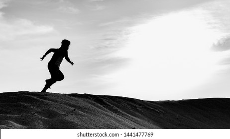 Pantai Klebang, Melaka - June 25, 2019: A Black And White Silhouette View Of A Young Man Running Freely At The Center Of Desert With Sunset As Background At Klebang Beach In Melaka.