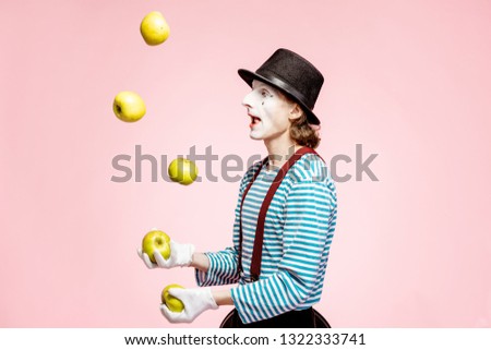Pantomime with white facial makeup juggling with apples on the pink background in the studio