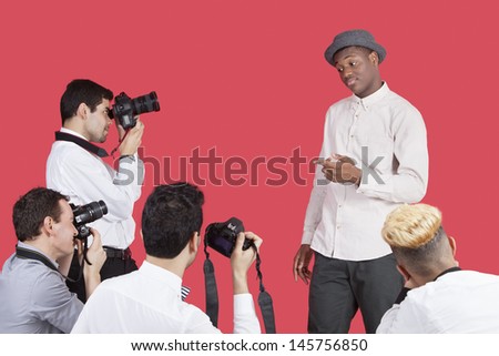 Paparazzi taking photographs of male actor over red background