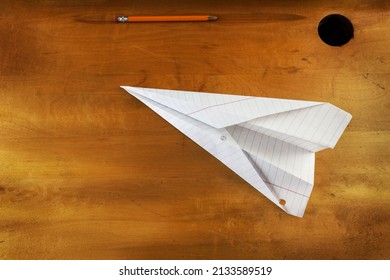 Paper Airplane Lying On A Vintage Wooden School Desk With A Pencil And Inkwell