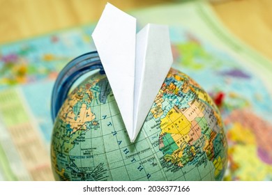 Paper Airplane On A Globe On The Background Of A World Map Travel Tourism Concept. High Quality Photo