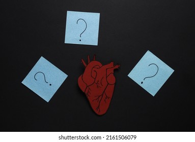 Paper Anatomical Heart With Question Marks On Memo Papers. Black Background. The Concept Of Diagnosis And Treatment Of Heart Disease