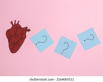 Paper Anatomical Heart With Question Marks On Memo Papers. Pink Background. The Concept Of Diagnosis And Treatment Of Heart Disease