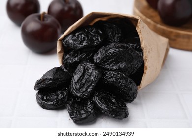 Paper bag with delicious prunes and fresh ripe plums on white tiled table, closeup