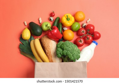 Paper bag with different groceries on coral background, flat lay