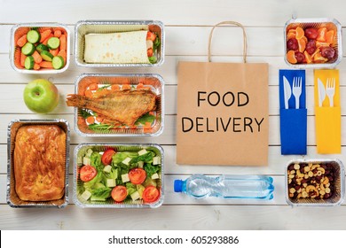 Paper Bag With Food Delivery Sign. Vegetable Roll, Baby Carrots And Cucumber, An Apple, A Pie, A Fish, Tomato And Lettuce Salad, A Bottle Of Water, Nuts, Plums And Cutlery. Tasty Meal Service.